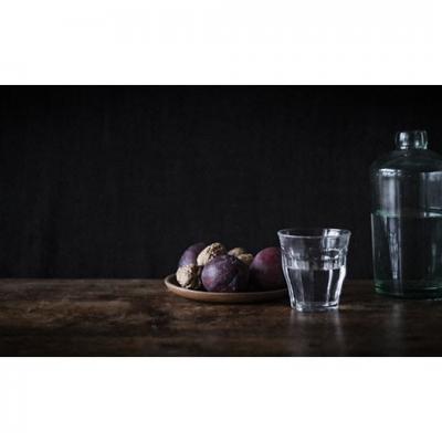 Des prunes sur une coupelle, un verre et une bouteille d'eau